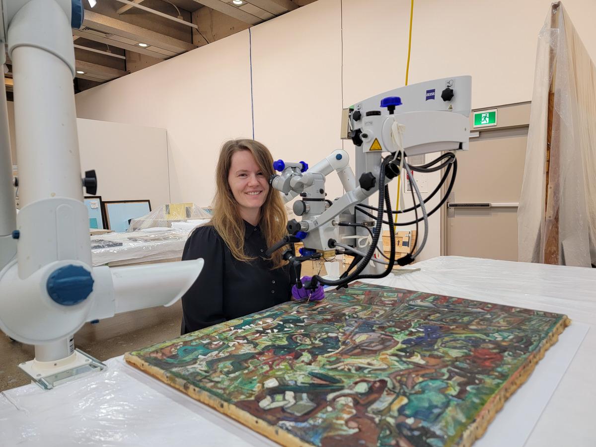 A photo of Christina McLean-Al Saidi working on Pegi Nicol MacLeod's painting Main Street, Fredericton (1941)