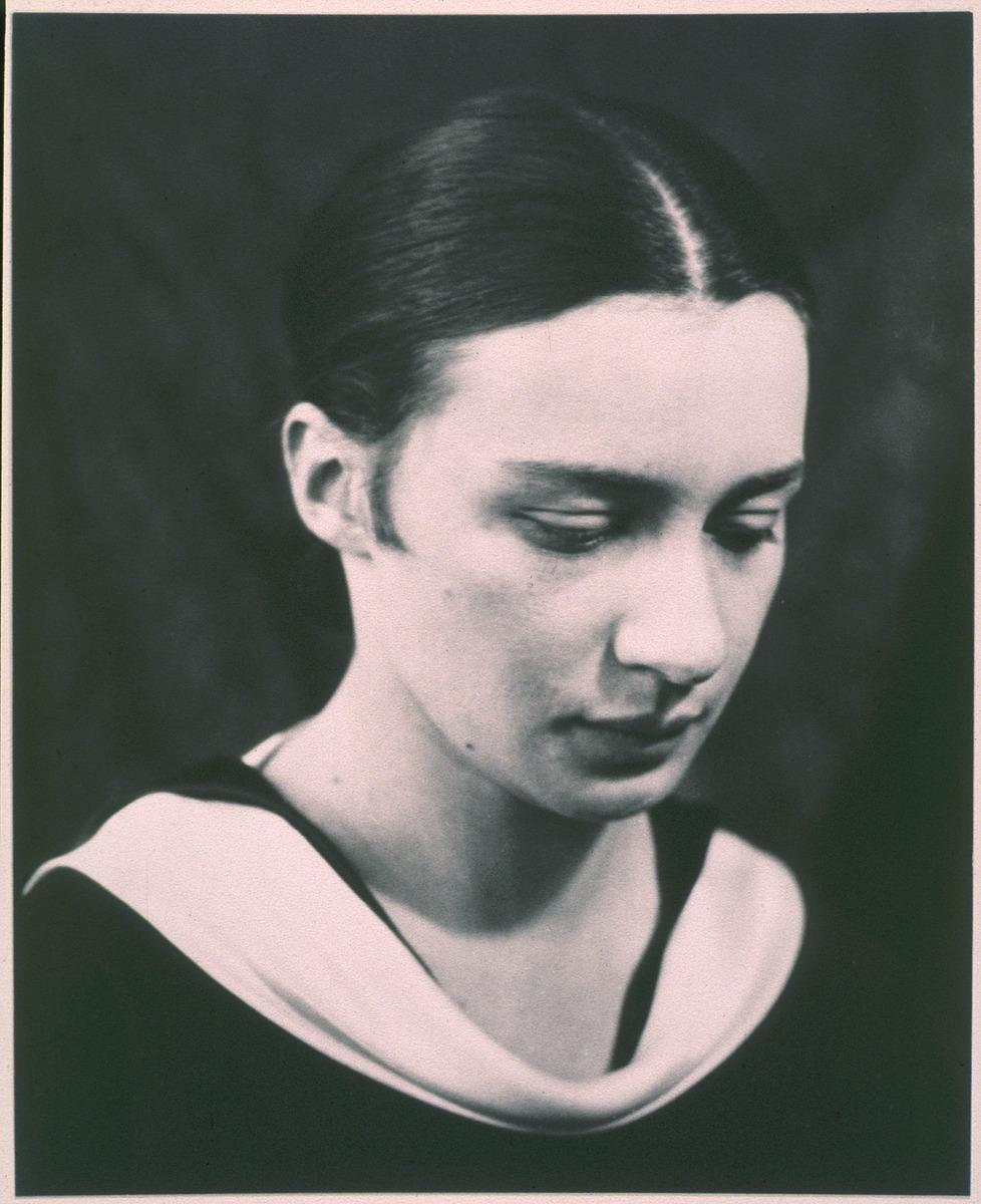 A young woman with her hair in a sleek bun and a neutral facial expression.