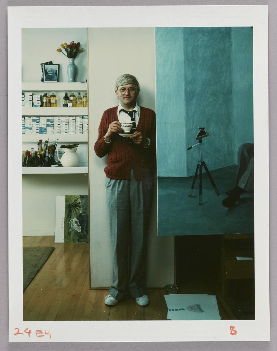 A photograph of a man standing in front of a wall holding a tea cup in his hand
