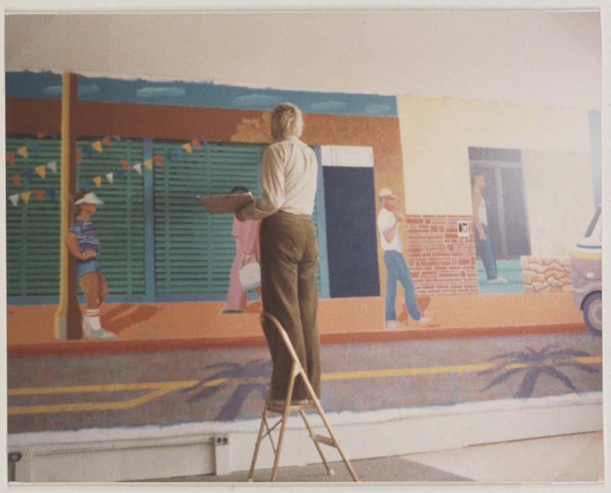 A man stands in front of a large horizontal painting on the wall behind him