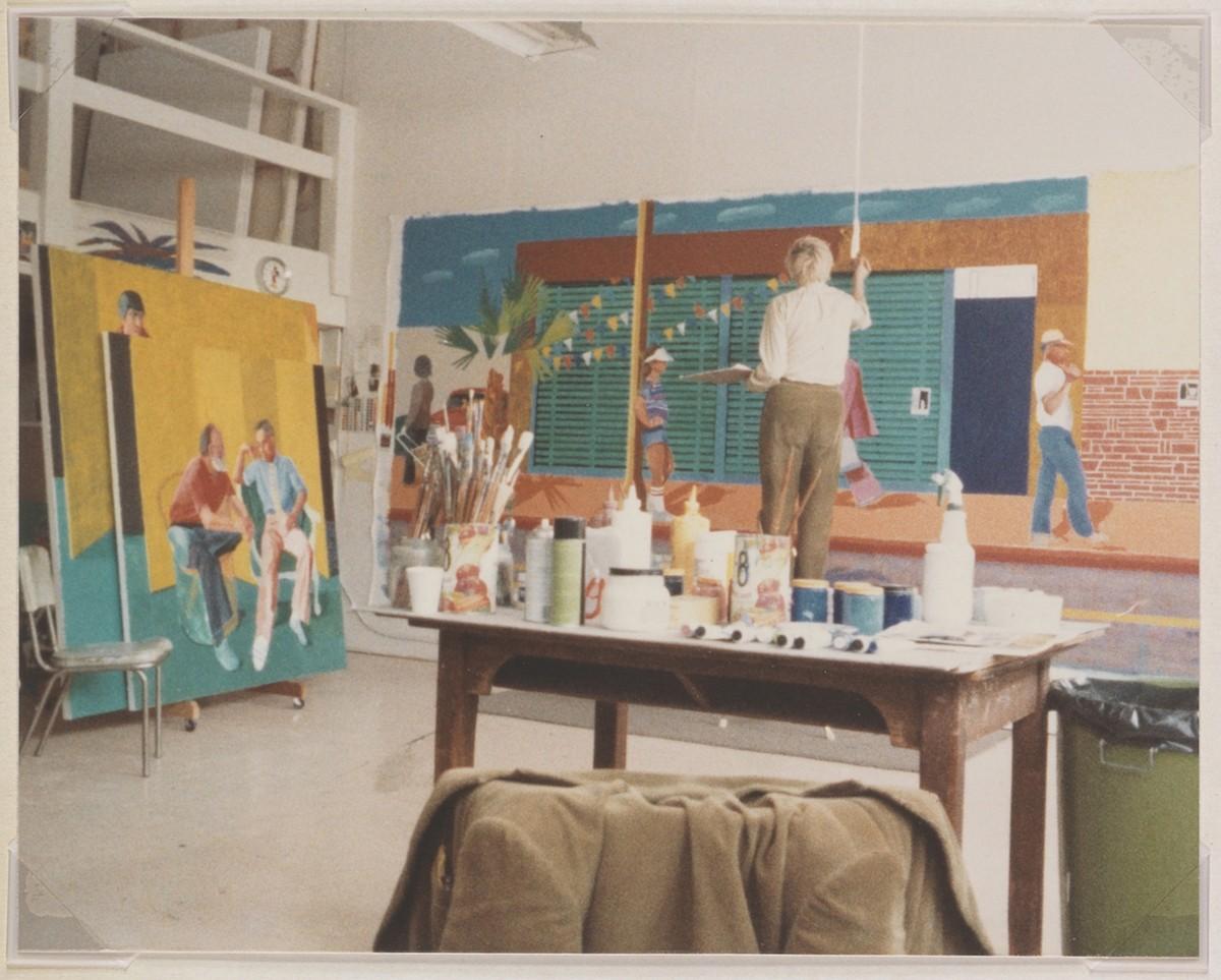 A man stands in front of a large horizontal painting on the wall behind him