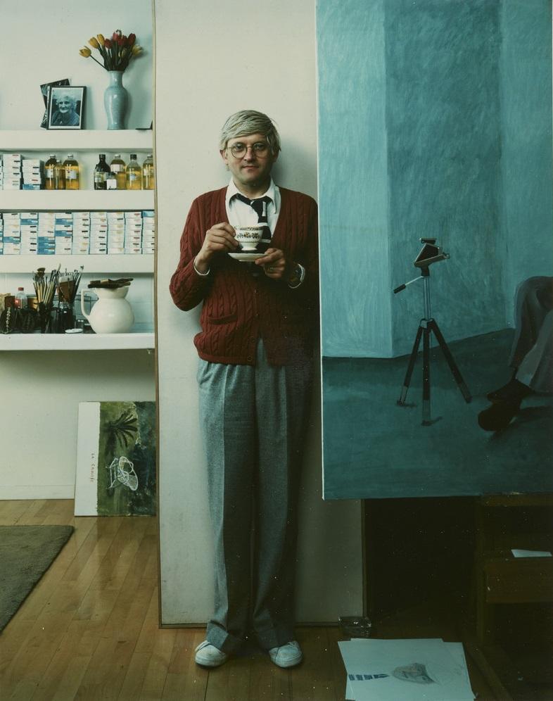 A photograph of a man standing in front of a wall holding a tea cup in his hand
