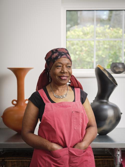 A photograph of Magdalene Odundo in front of two of her works 